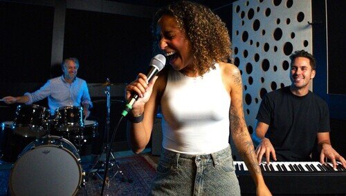 chanteuse qui répéte de manière énérgique avec un pianiste et un batteur dans un studio à Bruxelles