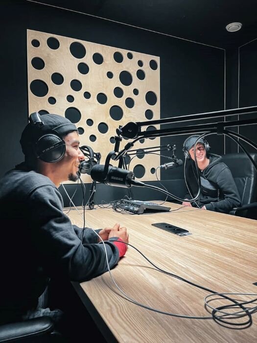 Studio de podcast avec deux animateurs souriants autour d'une table équipée de micros à Bruxelles