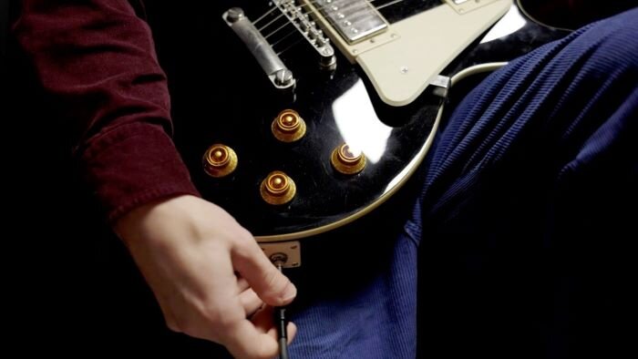 Guitare noire avec des boutons cuivrés et musicien branchant un jack à la guitare