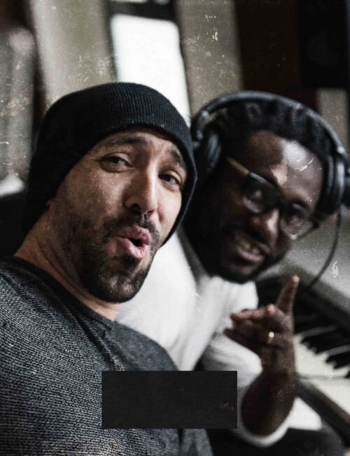 Two male artists seated in a recording studio in front of a piano keyboard. | © Plug The Jack