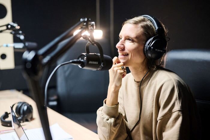 woman in front of a Shure MV7 podcast microphone, talking with headphones on. | © Plug The Jack