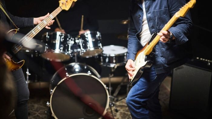 Energetic band rehearsing in a music rehearsal room with bassist, guitarist, and drummer. | © Plug The Jack