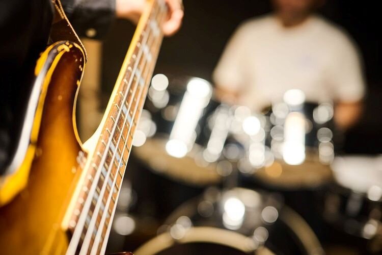 vintage bass neck, with a drummer sitting behind his drum kit in the background. | © Plug The Jack