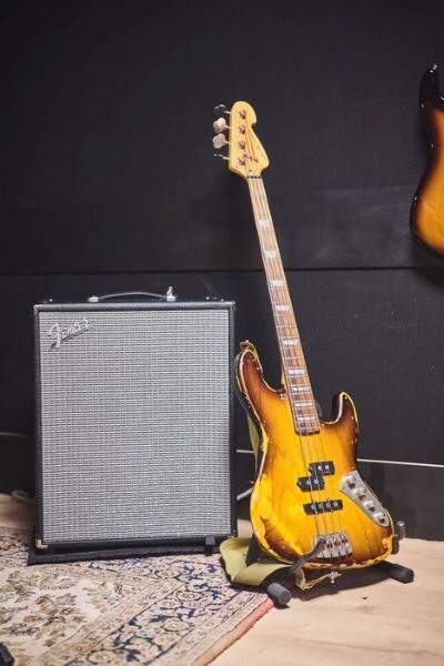 Oude houten bas tegen een Fender Rumble 200-versterker in een muziekrepetitiestudio. | © Plug The Jack