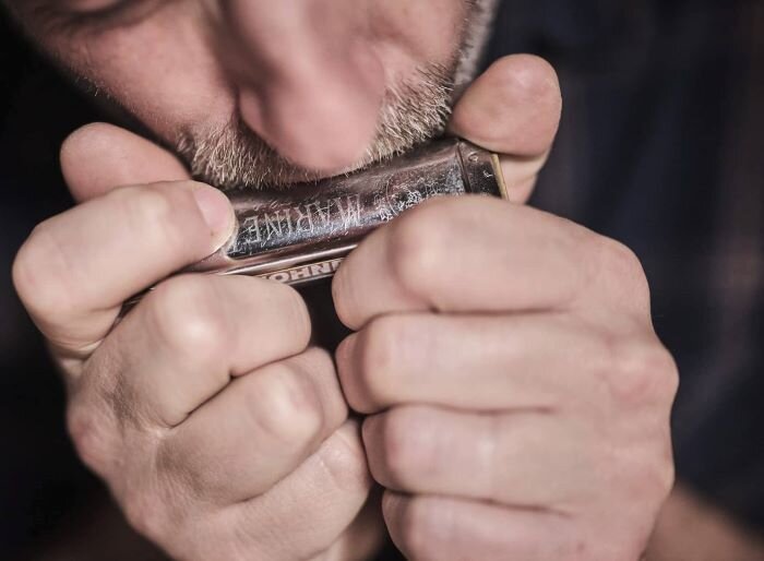 Muzikant die een mondharmonica voor zijn mond houdt. | © Plug The Jack